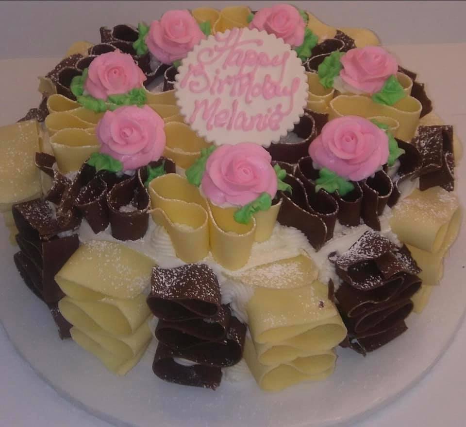 A birthday cake decorated with roses and chocolate swirls.