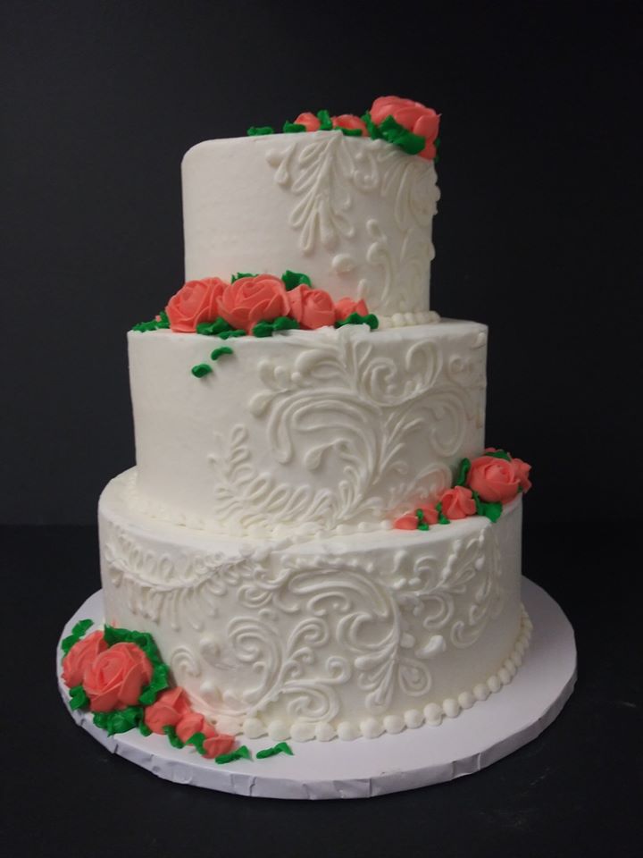 A white wedding cake with orange roses on top.
