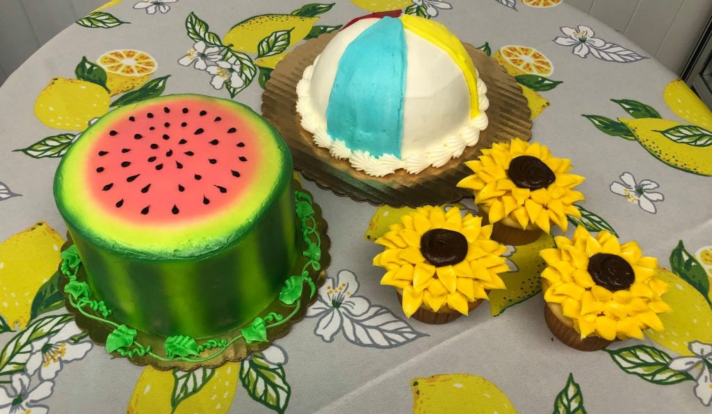 A cake with a watermelon, sunflowers, and cupcakes.