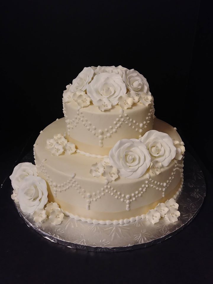 A white wedding cake with white roses on top.