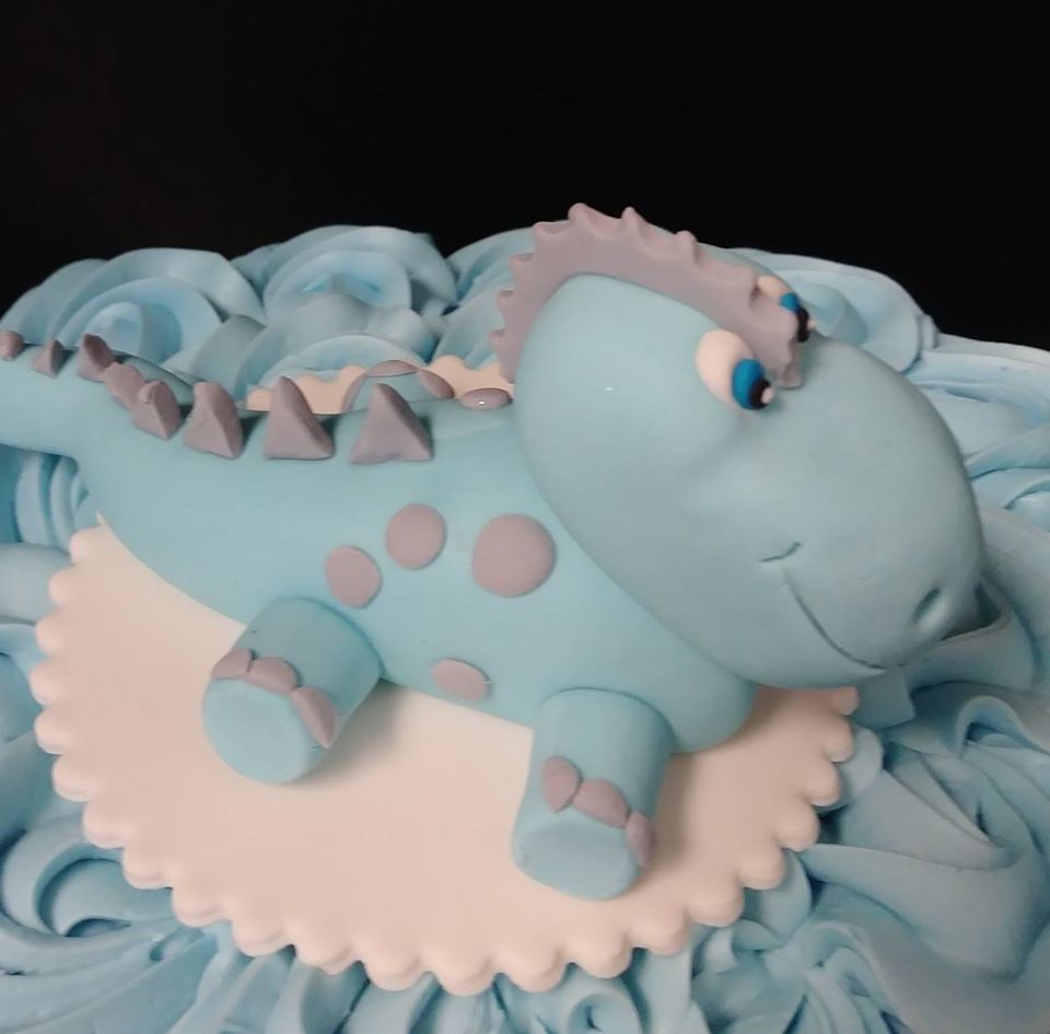 A blue cake with a blue dinosaur on top.