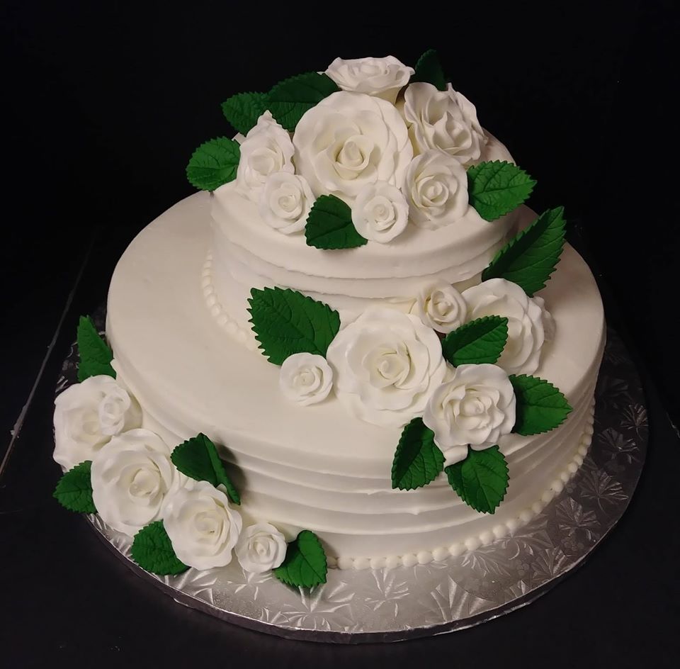 A white cake with green leaves and white roses.