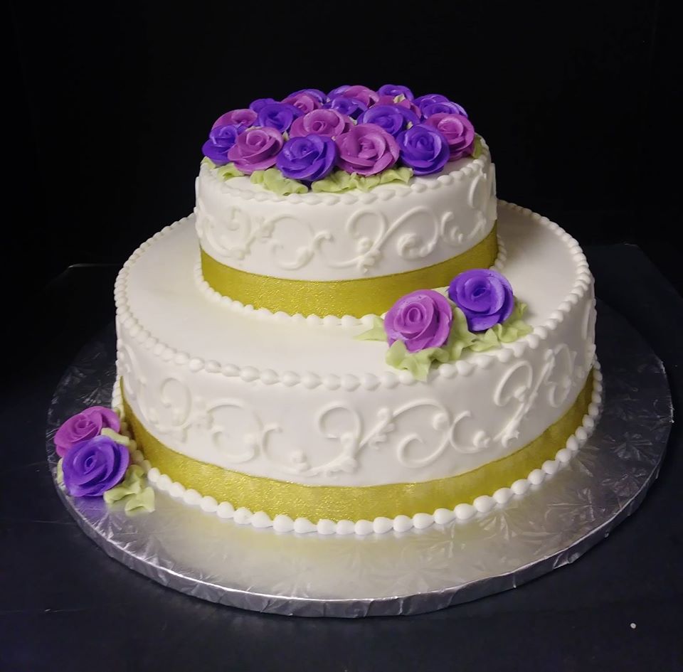 A white cake with purple roses on top.