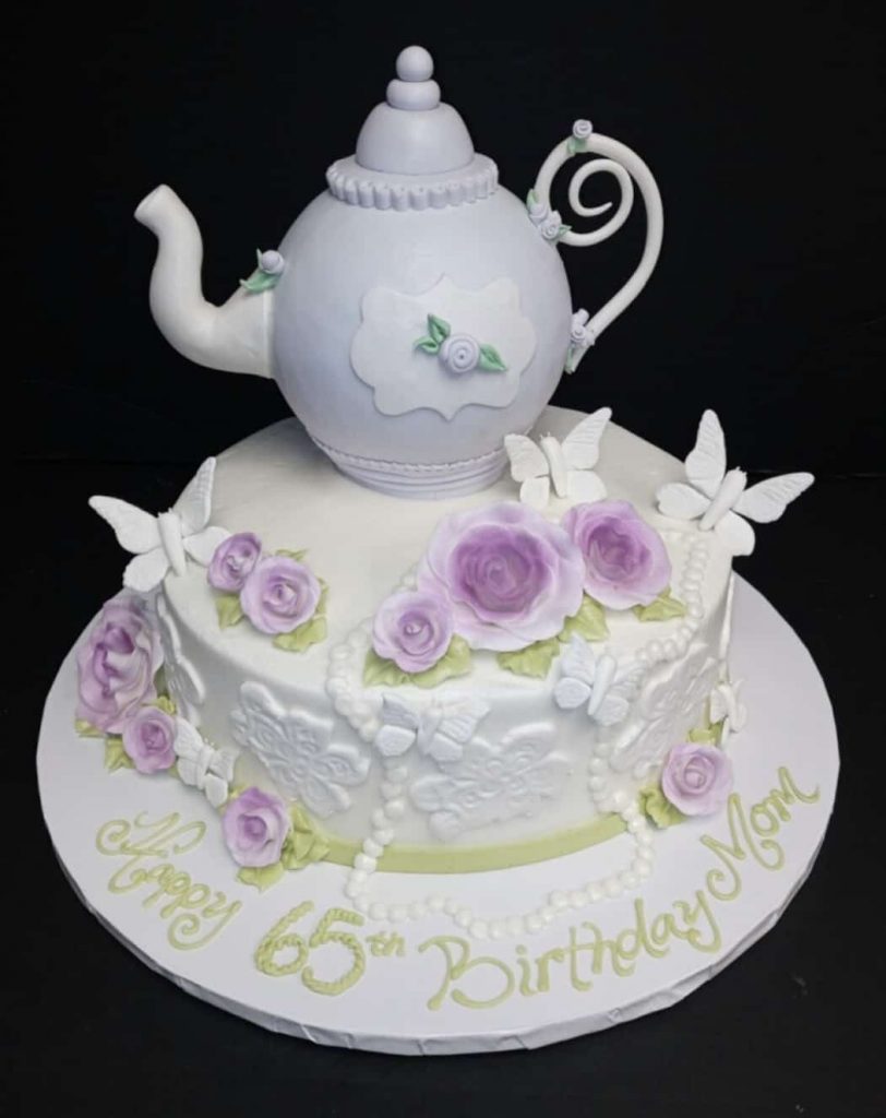 A cake with a teapot and flowers on top.