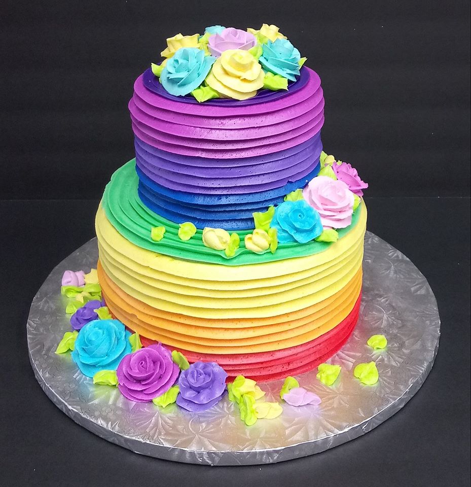 A rainbow - colored cake with roses on top.
