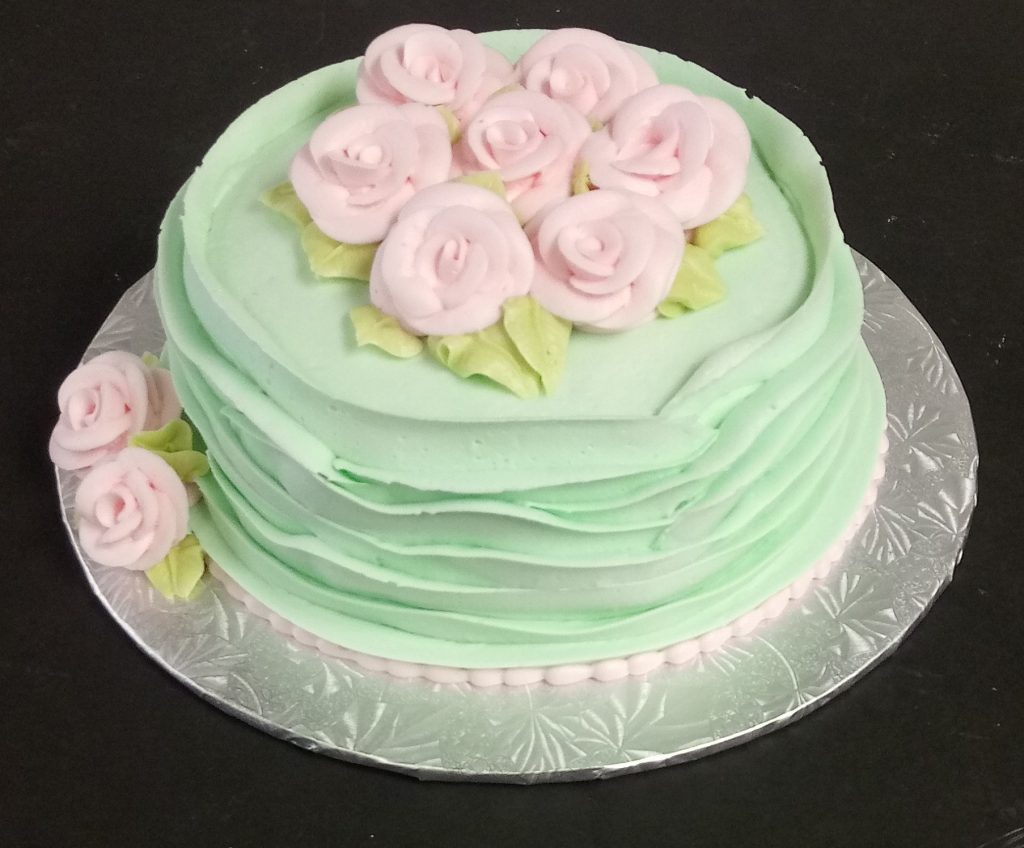 A green cake with pink roses on top.