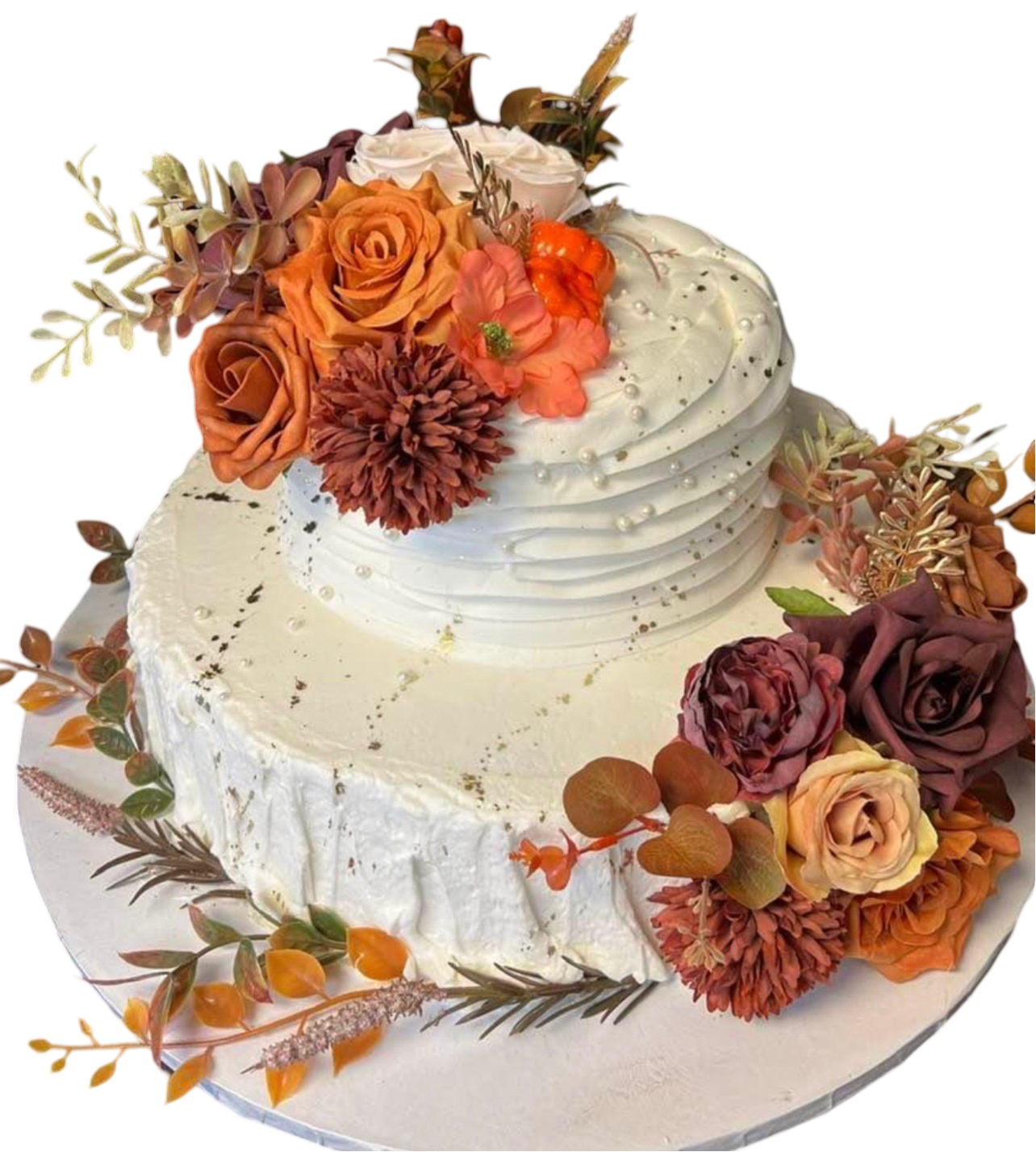 Two-tiered cake with white frosting, topped with orange, rust, and cream flowers, and autumn leaves.